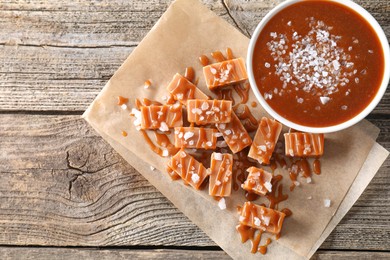 Caramel sauce with sea salt and yummy candies on wooden table, flat lay