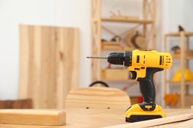 One cordless electric drill on wooden table in workshop. Space for text