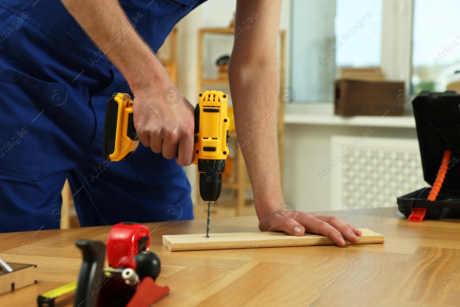 Photo of Craftsman working with drill at wooden table in workshop, closeup