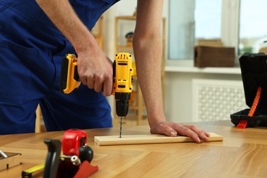 Craftsman working with drill at wooden table in workshop, closeup