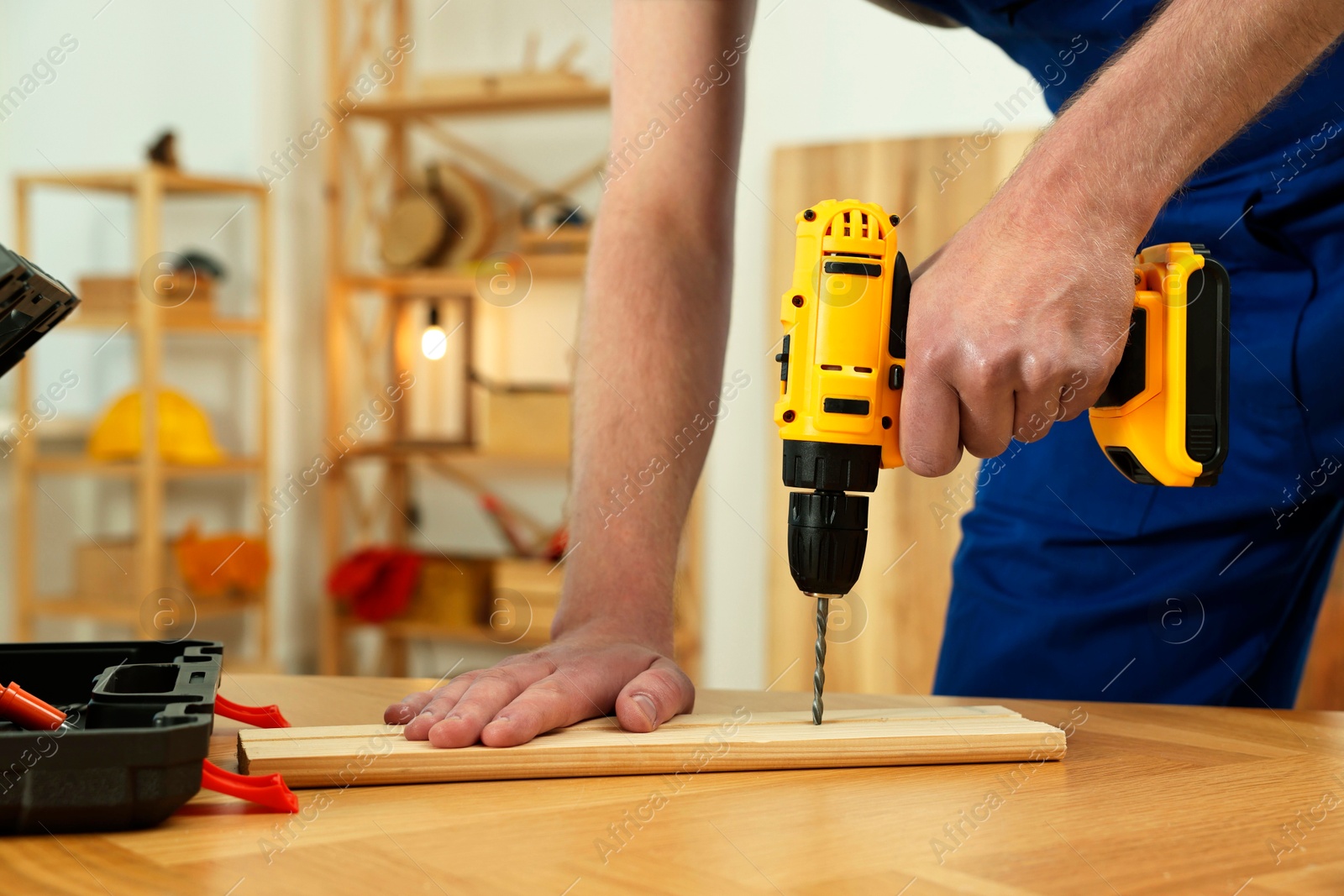 Photo of Craftsman working with drill at wooden table in workshop, closeup