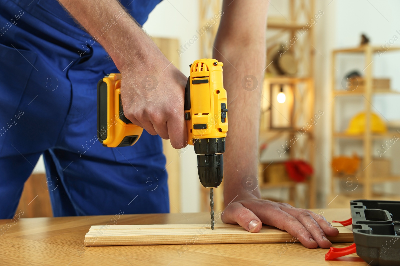 Photo of Craftsman working with drill at wooden table in workshop, closeup