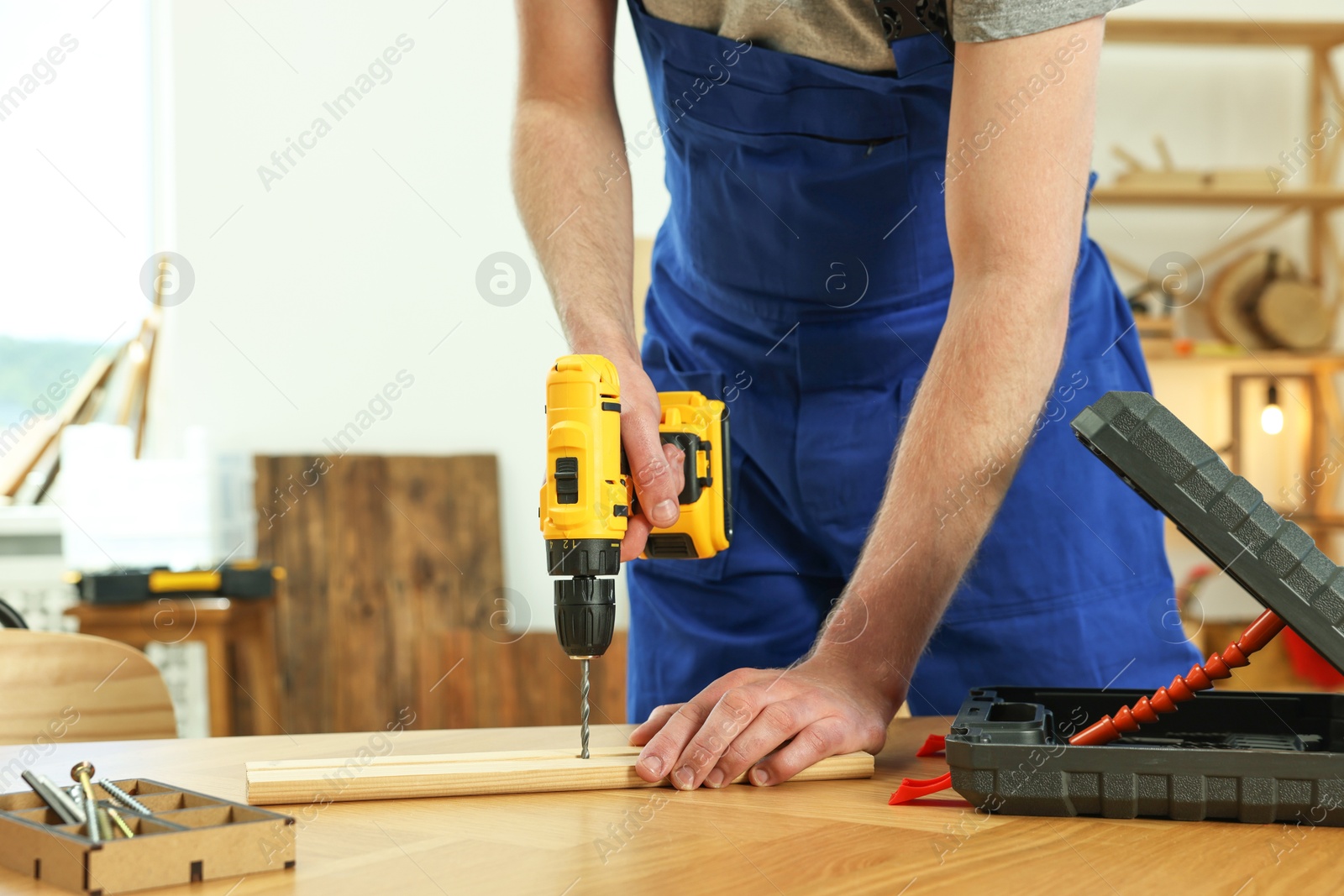 Photo of Craftsman working with drill at wooden table in workshop, closeup