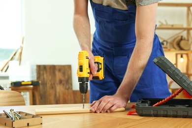 Craftsman working with drill at wooden table in workshop, closeup