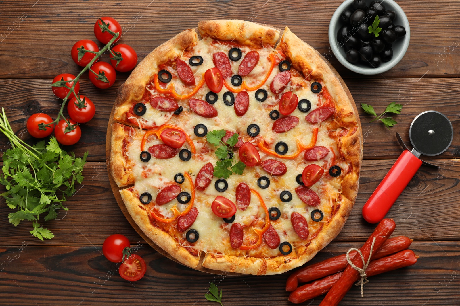 Photo of Tasty pizza, ingredients and cutter on wooden table, top view