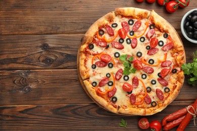 Photo of Tasty pizza with dry smoked sausages, tomatoes, olives, pepper and parsley on wooden table, top view. Space for text