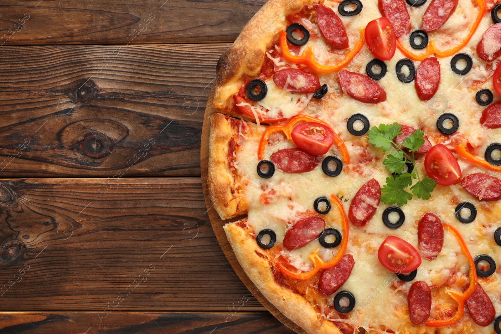 Photo of Tasty pizza with dry smoked sausages, tomato, olives, pepper and parsley on wooden table, top view. Space for text