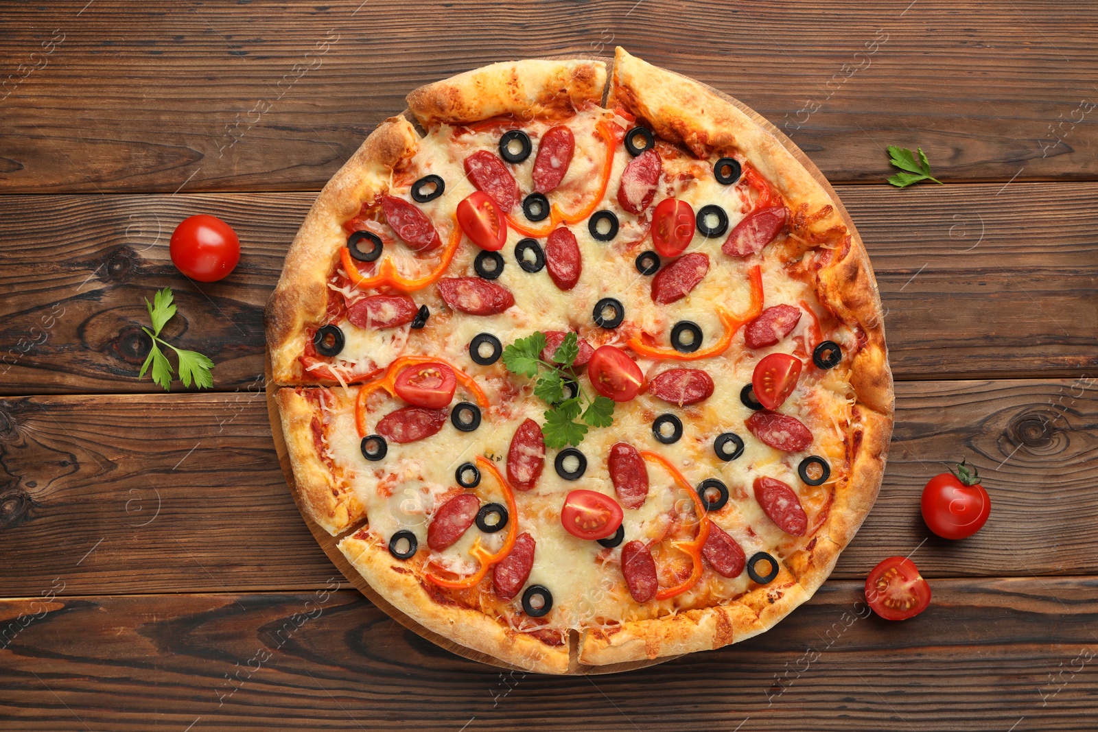 Photo of Tasty pizza with dry smoked sausages, tomatoes, olives, pepper and parsley on wooden table, top view