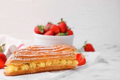 Photo of Delicious eclairs filled with cream and strawberries on white marble table