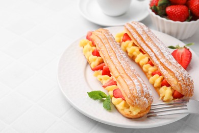 Photo of Delicious eclairs filled with cream, strawberries and mint on white tiled table, closeup. Space for text