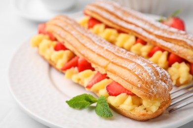 Photo of Delicious eclairs filled with cream, strawberries and mint on table, closeup