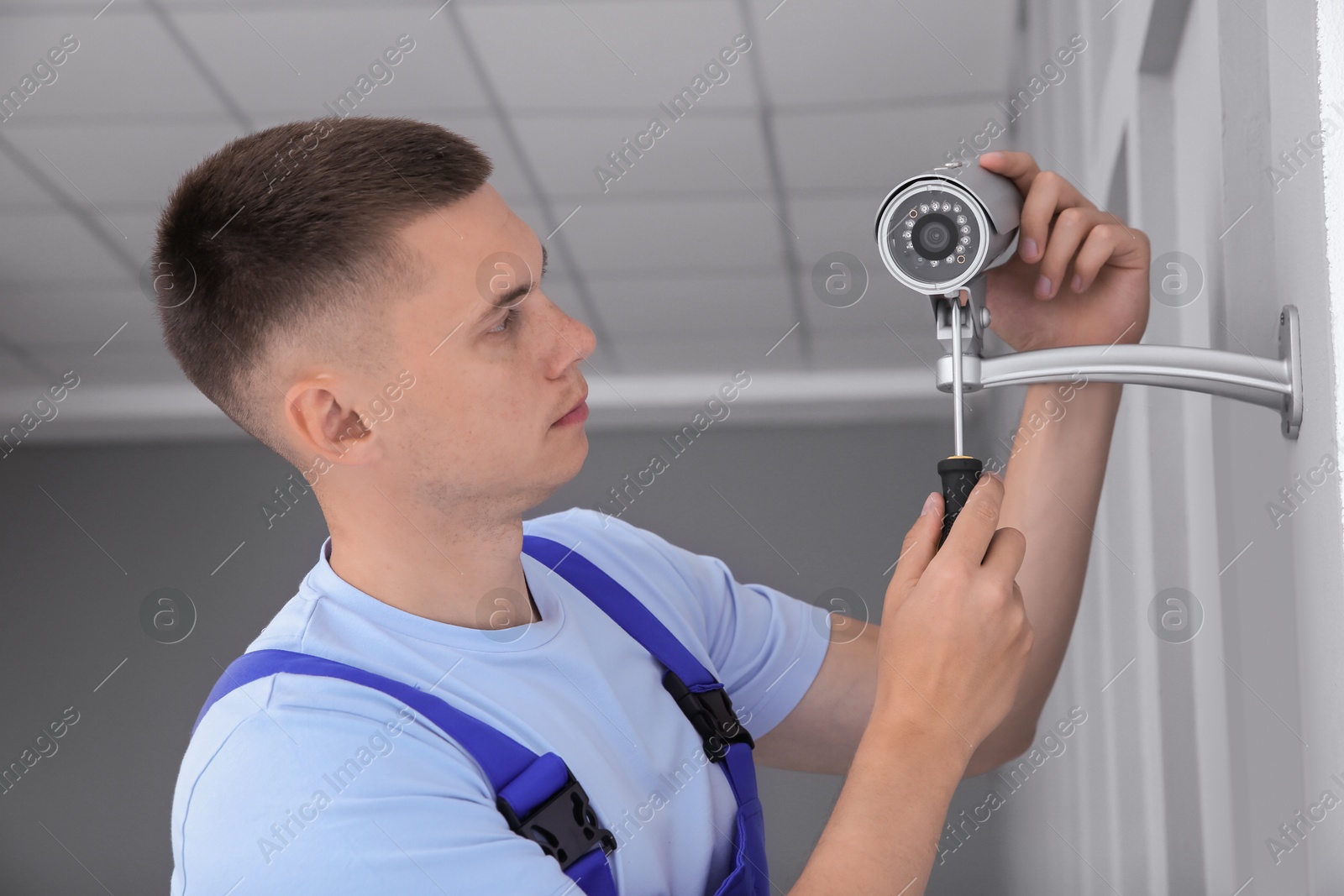 Photo of Technician with screwdriver installing CCTV camera on wall indoors