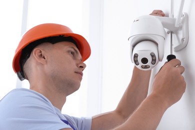 Technician with screwdriver installing CCTV camera on wall indoors