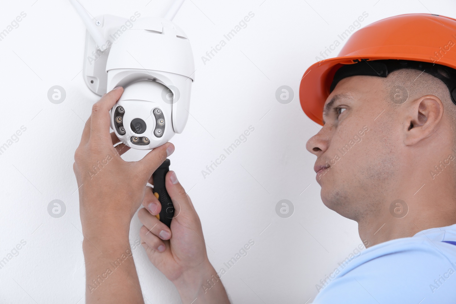 Photo of Technician with screwdriver installing CCTV camera on wall indoors