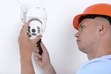 Technician with screwdriver installing CCTV camera on wall indoors