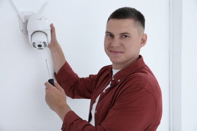 Photo of Technician with screwdriver installing CCTV camera on wall indoors