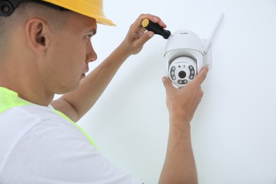 Photo of Technician with screwdriver installing CCTV camera on wall indoors, closeup