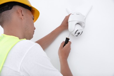 Technician with screwdriver installing CCTV camera on wall indoors