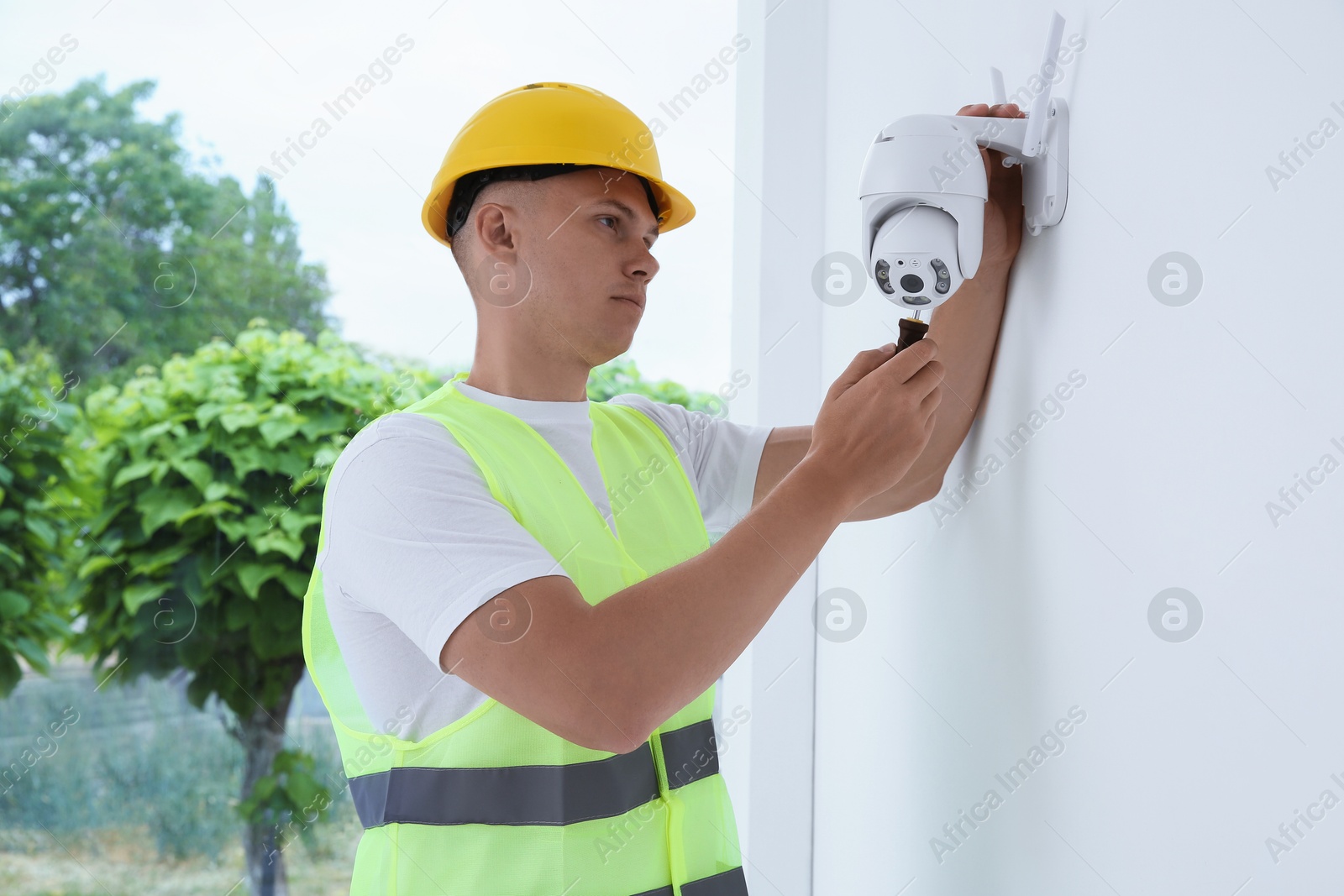 Photo of Technician with screwdriver installing CCTV camera on wall indoors