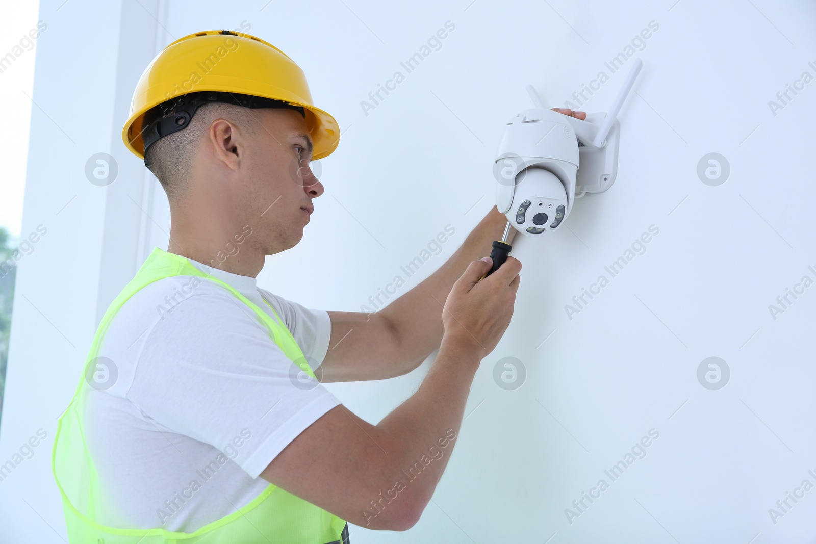 Photo of Technician with screwdriver installing CCTV camera on wall indoors