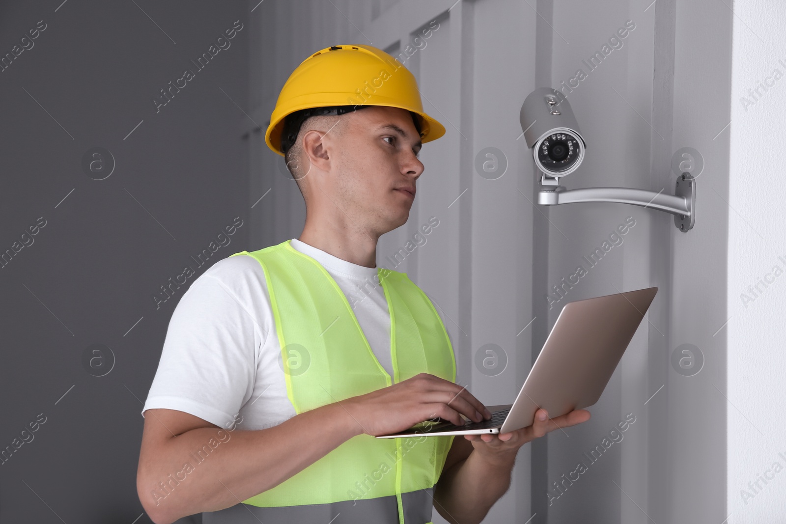 Photo of Technician with laptop installing CCTV camera indoors