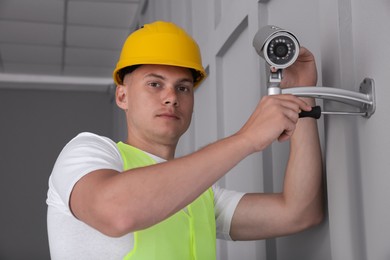 Technician with screwdriver installing CCTV camera on wall indoors