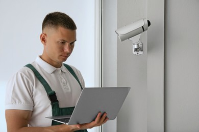 Technician with laptop installing CCTV camera indoors