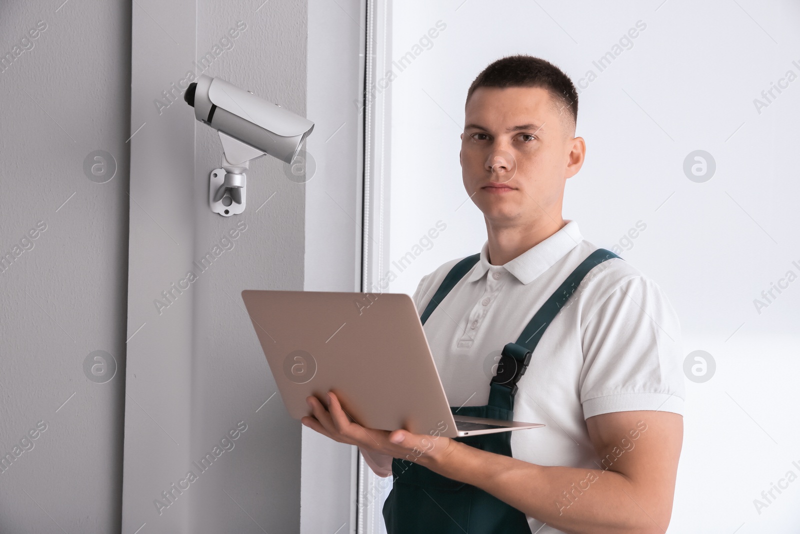 Photo of Technician with laptop installing CCTV camera indoors