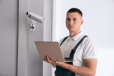 Technician with laptop installing CCTV camera indoors