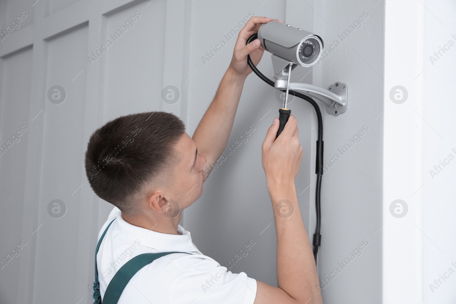 Photo of Technician with screwdriver installing CCTV camera on wall indoors