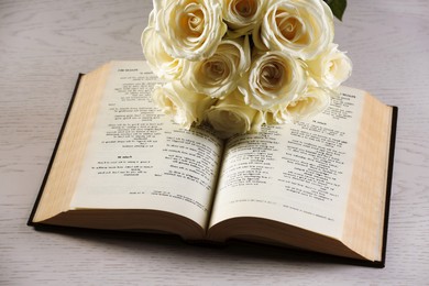 Photo of Bible and roses on light wooden table, closeup. Religion of Christianity
