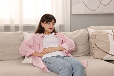 Photo of Upset woman suffering from abdominal pain on sofa at home