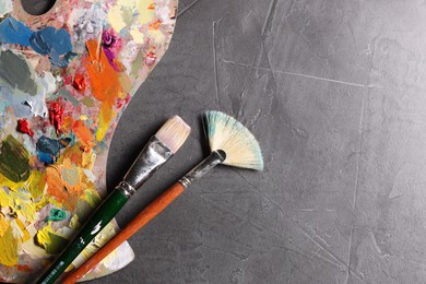 Photo of Artist's palette, brushes and paints on grey table, flat lay. Space for text