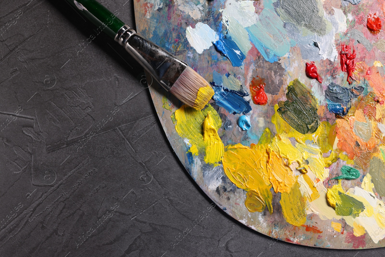 Photo of Artist's palette, brush and paints on grey table, top view. Space for text