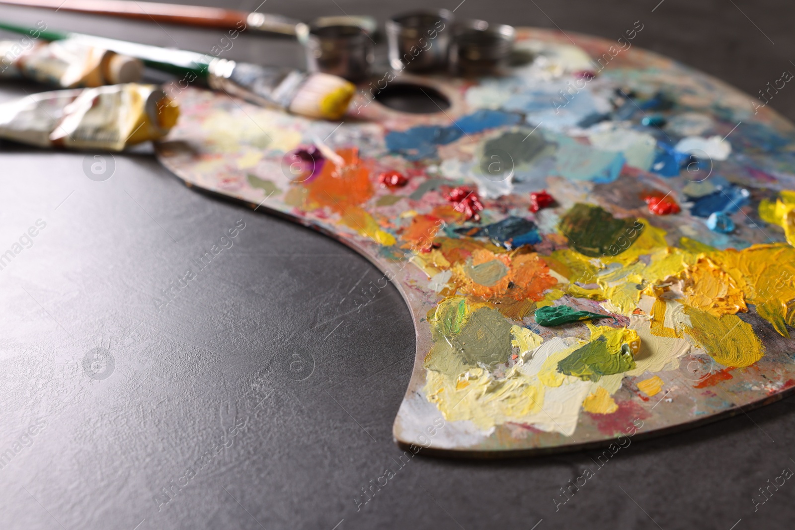Photo of Artist's palette, brushes and paints on grey table, closeup. Space for text