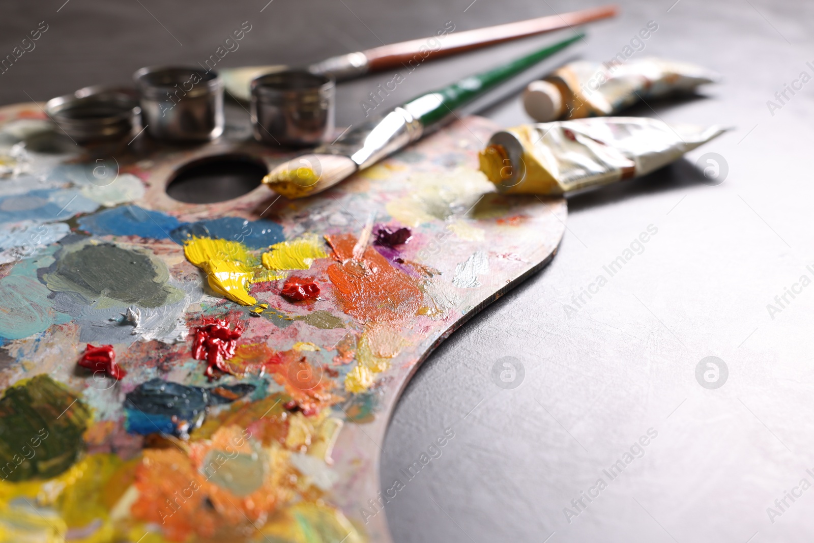 Photo of Artist's palette, brushes and paints on grey table, closeup. Space for text