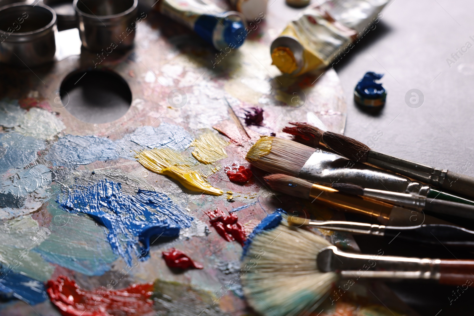 Photo of Artist's palette, brushes and paints on grey table, closeup