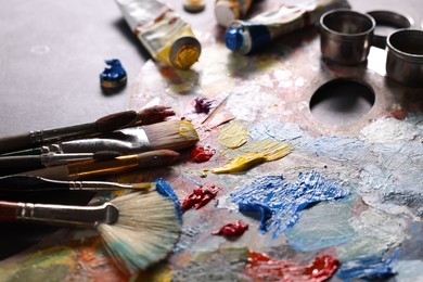 Artist's palette, brushes and paints on grey table, closeup