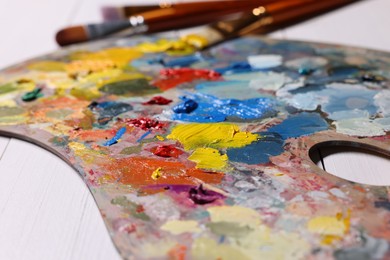 Artist's palette, brushes, paints on white wooden table, closeup