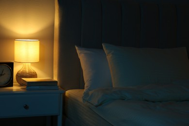 Nightlight, clock and books on bedside table near bed indoors
