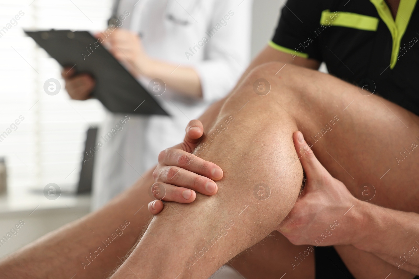 Photo of Sportsman holding injured leg while doctor filling documents in hospital, closeup