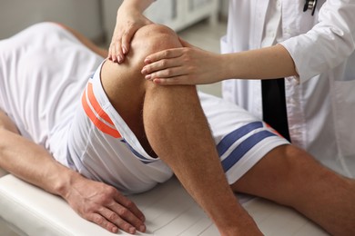 Photo of Sports injury. Doctor examining patient's knee in hospital, closeup