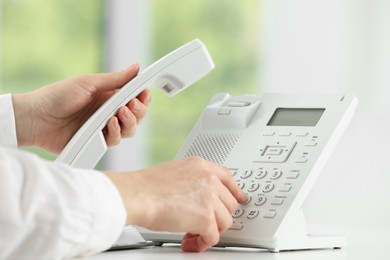 Assistant dialing number on telephone against blurred background, closeup