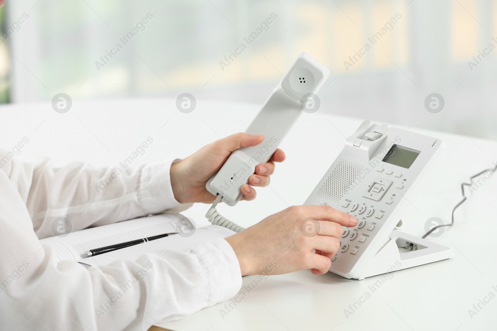 Photo of Assistant dialing number on telephone against blurred background, closeup