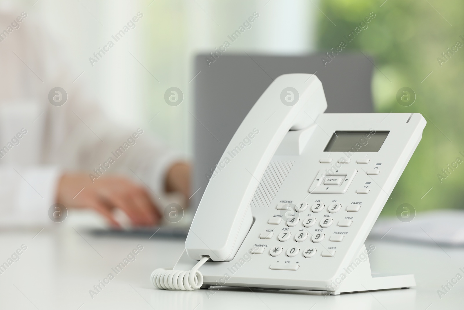 Photo of White telephone on table against blurred background, selective focus