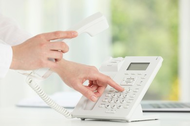 Assistant dialing number on telephone against blurred green background, closeup