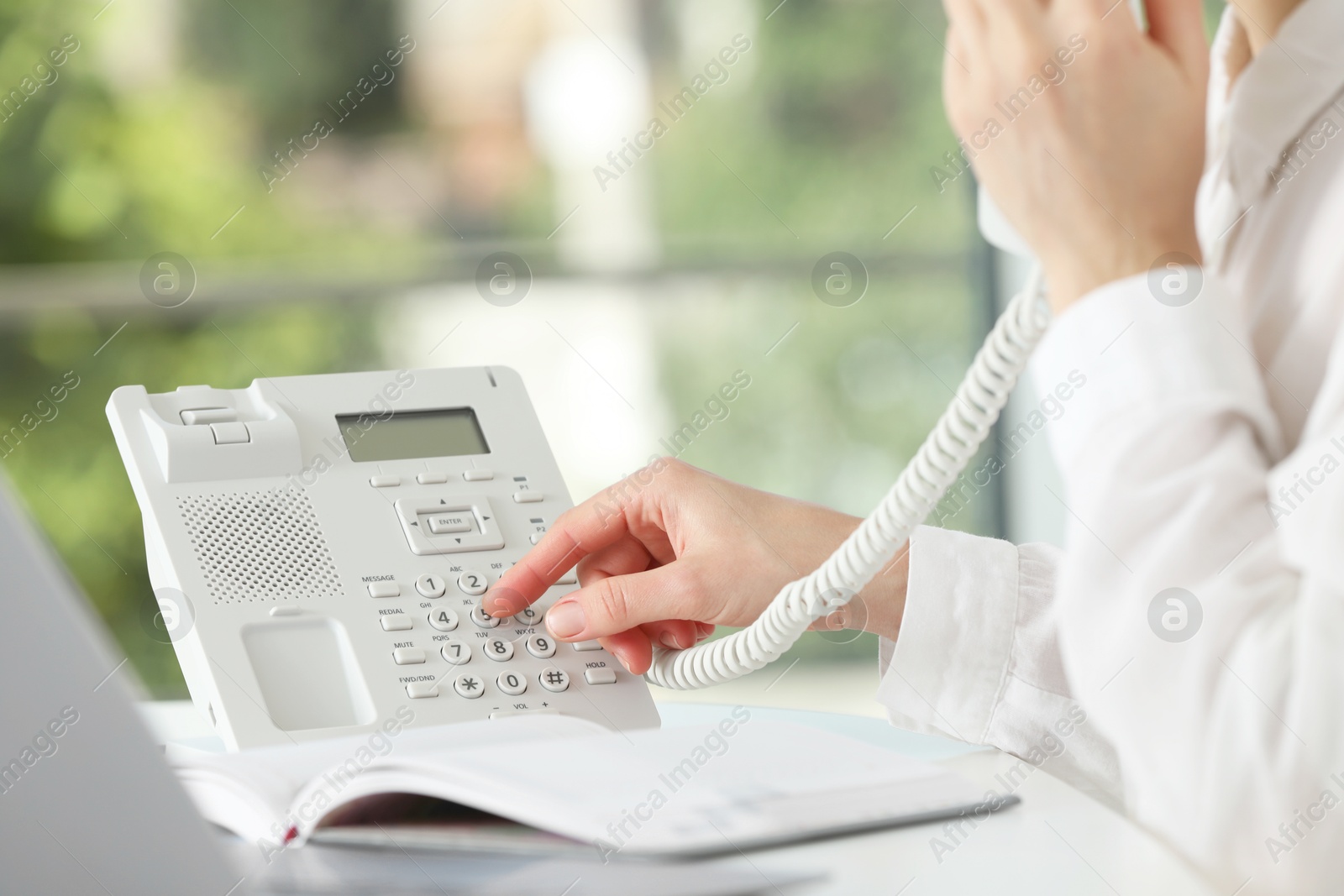 Photo of Assistant dialing number on telephone at table against blurred green background, closeup