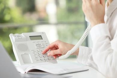 Assistant dialing number on telephone at table against blurred green background, closeup