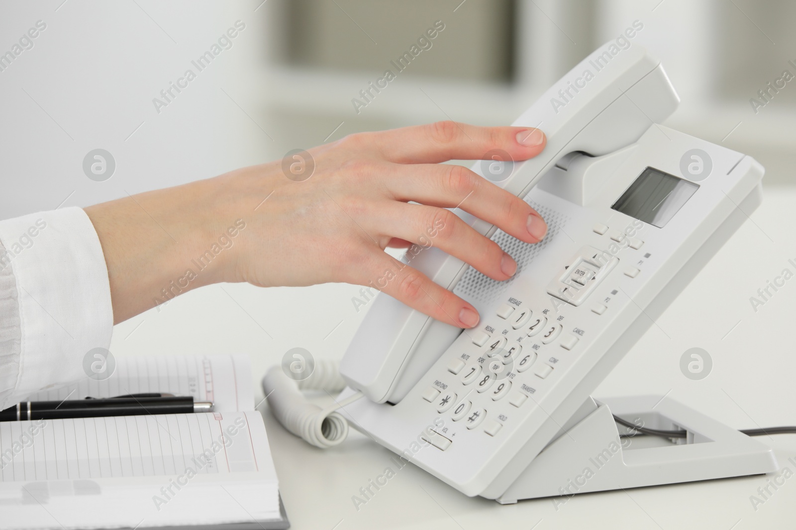 Photo of Assistant taking telephone handset at white table, closeup