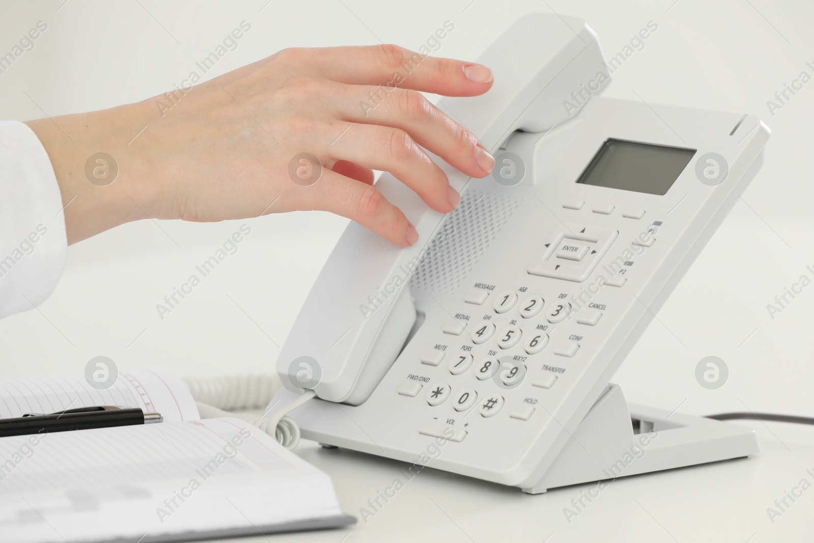 Photo of Assistant taking telephone handset at white table, closeup